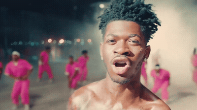 A Man Without A Shirt Is Standing In Front Of A Crowd Of People In Pink Pants GIF