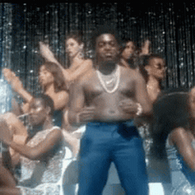 A Man Without A Shirt Is Standing In Front Of A Crowd Of Women . GIF