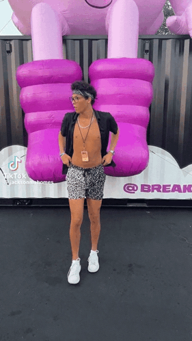 A Man Without A Shirt Is Standing In Front Of A Giant Inflatable Purple Elephant . GIF