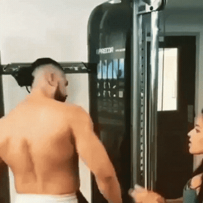 A Man Without A Shirt Is Standing In Front Of A Machine In A Gym . GIF