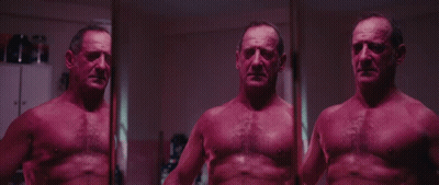 A Man Without A Shirt Is Standing In Front Of A Mirror And Looking At Himself GIF