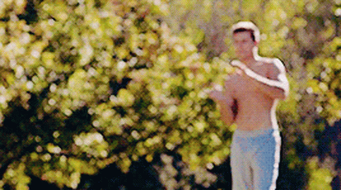 A Man Without A Shirt Is Standing In Front Of A Tree . GIF