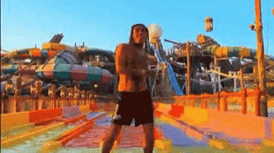 A Man Without A Shirt Is Standing In Front Of A Water Park . GIF