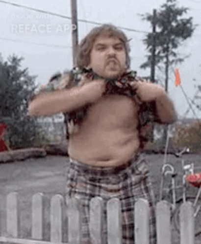A Man Without A Shirt Is Standing In Front Of A White Fence . GIF