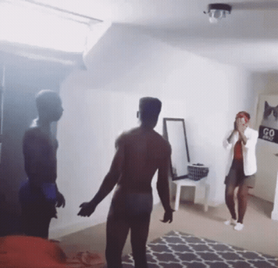 A Man Without A Shirt Is Standing In Front Of A Woman In A Room With A Sign That Says Go First GIF