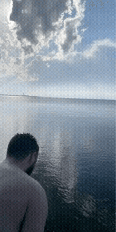 A Man Without A Shirt Is Standing In The Water Looking At The Ocean GIF
