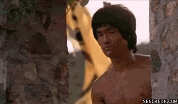A Man Without A Shirt Is Standing Next To A Brick Wall With A Dog Behind Him . GIF
