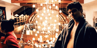 A Man Without A Shirt Is Standing Next To A Woman In A Room With A Christmas Tree In The Background . GIF