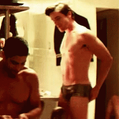 A Man Without A Shirt Is Standing Next To Another Man GIF