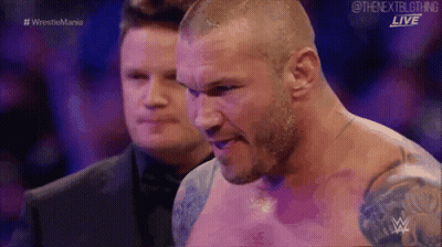 A Man Without A Shirt Is Standing Next To Another Man In A Wrestling Match . GIF