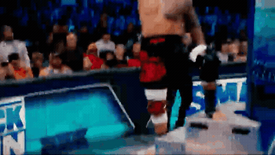 A Man Without A Shirt Is Standing On A Box In Front Of A Crowd At A Wrestling Match . GIF