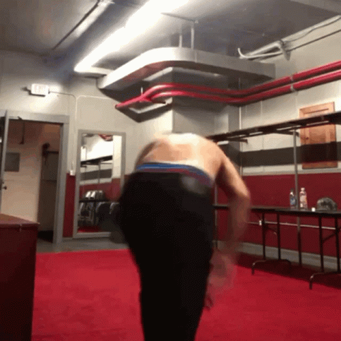 A Man Without A Shirt Is Standing On A Red Carpet In A Gym GIF