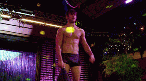 A Man Without A Shirt Is Standing On A Stage Holding A Jacket GIF