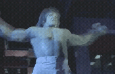 A Man Without A Shirt Is Standing On A Stage With His Arms Outstretched And Singing Into A Microphone . GIF
