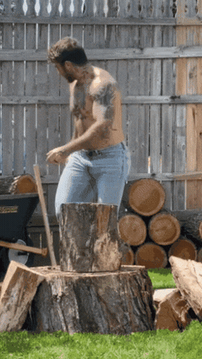 A Man Without A Shirt Is Standing On A Tree Stump With An Axe GIF
