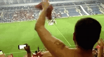 A Man Without A Shirt Is Taking A Picture Of A Soccer Game While A Crowd Watches . GIF