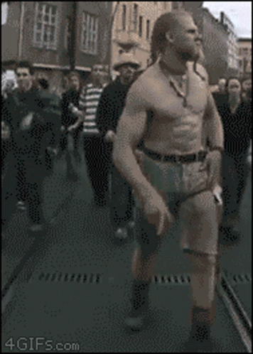 A Man Without A Shirt Is Walking Down A Street In Front Of A Crowd Of People With The Website 4Gifs.com Visible GIF