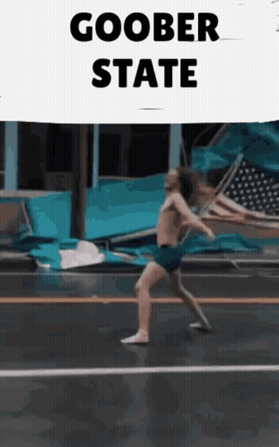 A Man Without A Shirt Is Walking Down A Street With A Sign That Says Goober State GIF