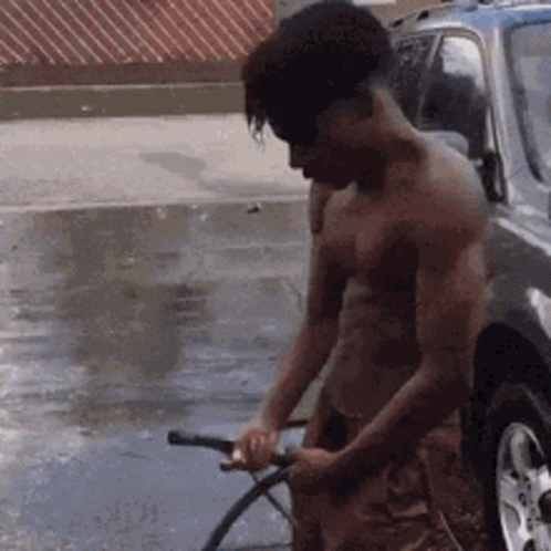 A Man Without A Shirt Is Washing A Car With A Hose GIF