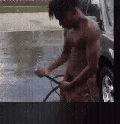 A Man Without A Shirt Is Washing A Car With A Hose . GIF