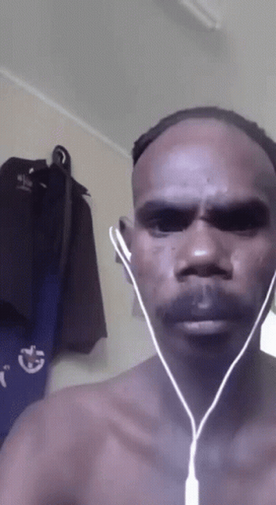 A Man Without A Shirt Is Wearing Ear Buds In Front Of A Wall With Clothes Hanging GIF