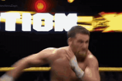 A Man Without A Shirt Is Wrestling In A Ring With The Word Tion Behind Him . GIF