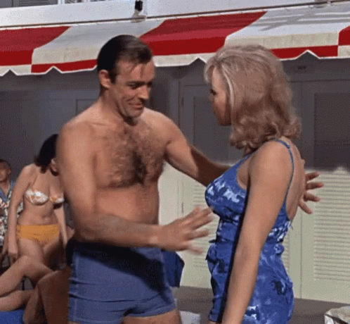A Man Without A Shirt Talks To A Woman In A Blue Dress GIF