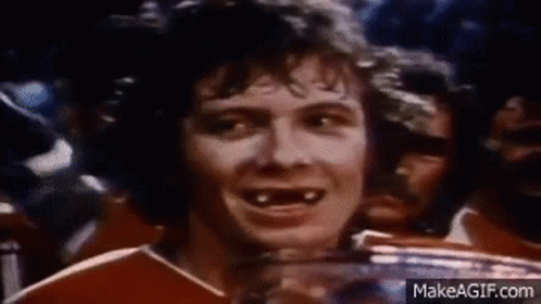 A Man Without Teeth Is Smiling While Holding A Trophy In Front Of A Crowd Of People . GIF