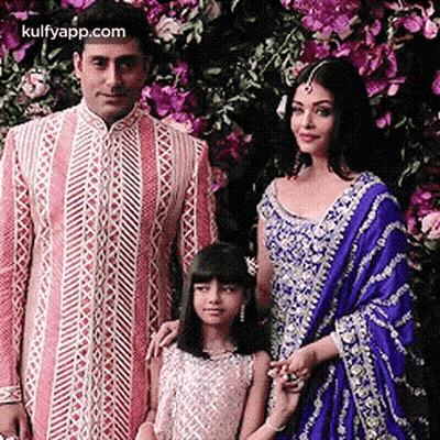 A Man , Woman , And Child Are Posing For A Picture In Front Of Flowers . GIF