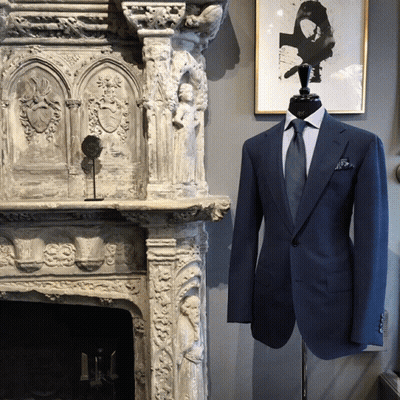 A Mannequin Wearing A Blue Suit And Tie Stands In Front Of A Stone Fireplace GIF