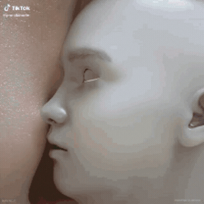 A Mannequin With Its Mouth Open Is Being Breastfed By A Woman . GIF