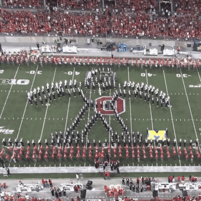 A Marching Band Is Performing On A Football Field With The Letter M On The Field GIF