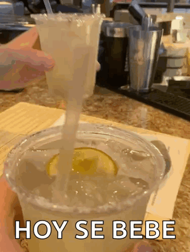 A Margarita Is Being Poured Into A Plastic Cup With A Straw And The Words Hoy Se Bebe On The Bottom GIF