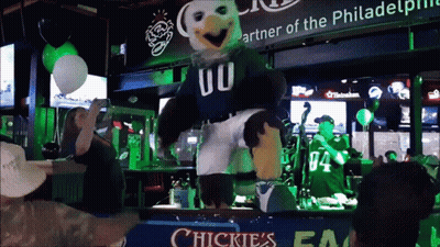 A Mascot Dancing In Front Of A Sign That Says Chickies GIF