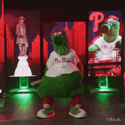 A Mascot For The Phillies Is Dancing In Front Of A Large Screen GIF