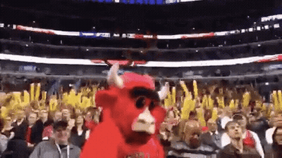 A Mascot In A Bull Costume Is Dancing In Front Of A Crowd Of People At A Basketball Game . GIF