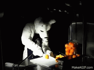 A Mascot Is Cutting Oranges On A Cutting Board GIF