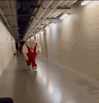 A Mascot Is Walking Down A Hallway With Pipes GIF