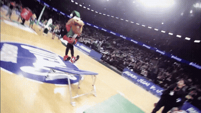 A Mascot Performs A Trick On A Trampoline In Front Of A Sign That Says ' Pecan ' On It GIF