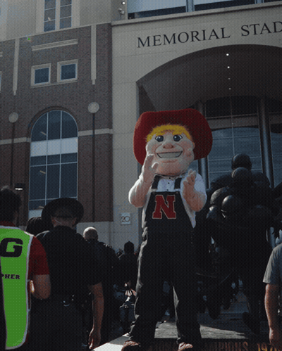 A Mascot Standing In Front Of A Building That Says Memorial Stadium GIF