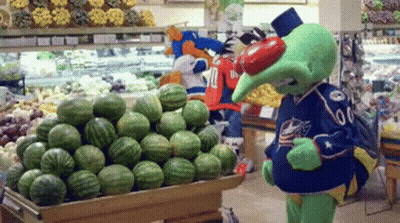 A Mascot Standing In Front Of A Display Of Watermelons GIF