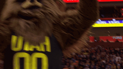 A Mascot Wearing A Utah Jersey Stands In Front Of A Crowd At A Basketball Game GIF