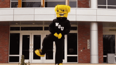 A Mascot Wearing A Wsu Sweatshirt Is Standing In Front Of A Building GIF
