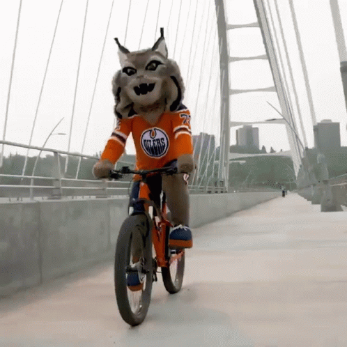 A Mascot Wearing An Edmonton Oilers Jersey Rides A Bike On A Bridge GIF