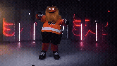 A Mascot With A Beard Is Holding A Hockey Puck In Front Of A Sign That Says ' Flyers ' GIF