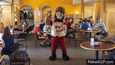 A Mascot With The Letter D On His Shirt Stands In A Restaurant GIF
