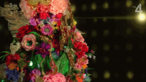 A Masked Singer Costume With Flowers And Leaves On It GIF