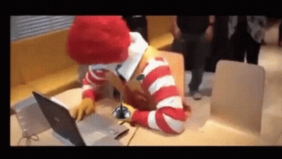 A Mcdonald 'S Clown Is Sitting At A Table Using A Laptop Computer GIF