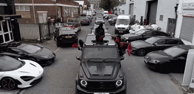 A Mercedes Benz G63 Is Driving Down A Street Surrounded By Lots Of Cars . GIF