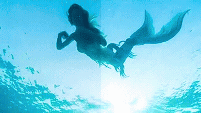 A Mermaid Is Swimming In The Ocean With The Sun Behind Her . GIF